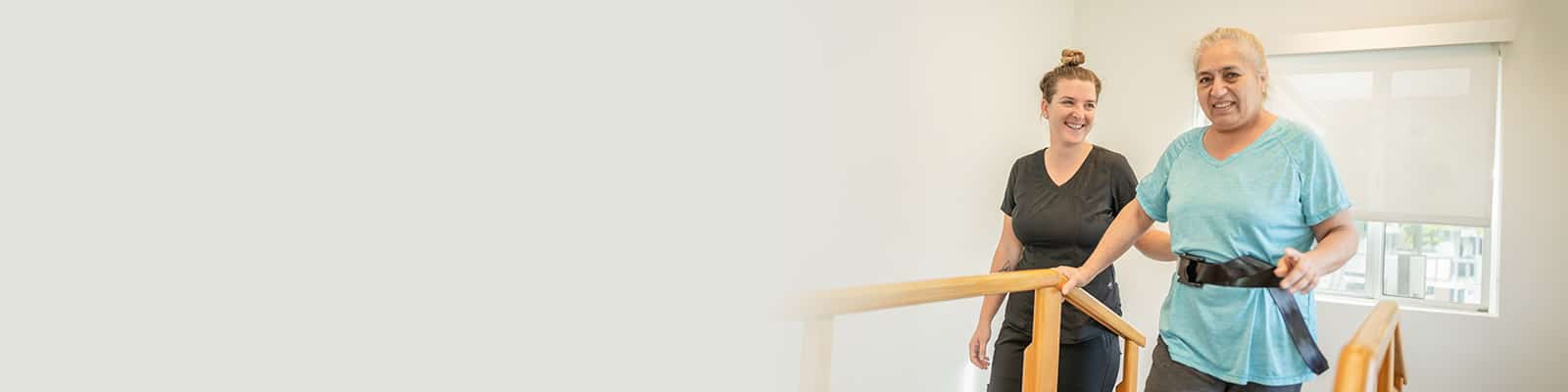 A rehab therapist with a resident holding railings in the physical therapy gym